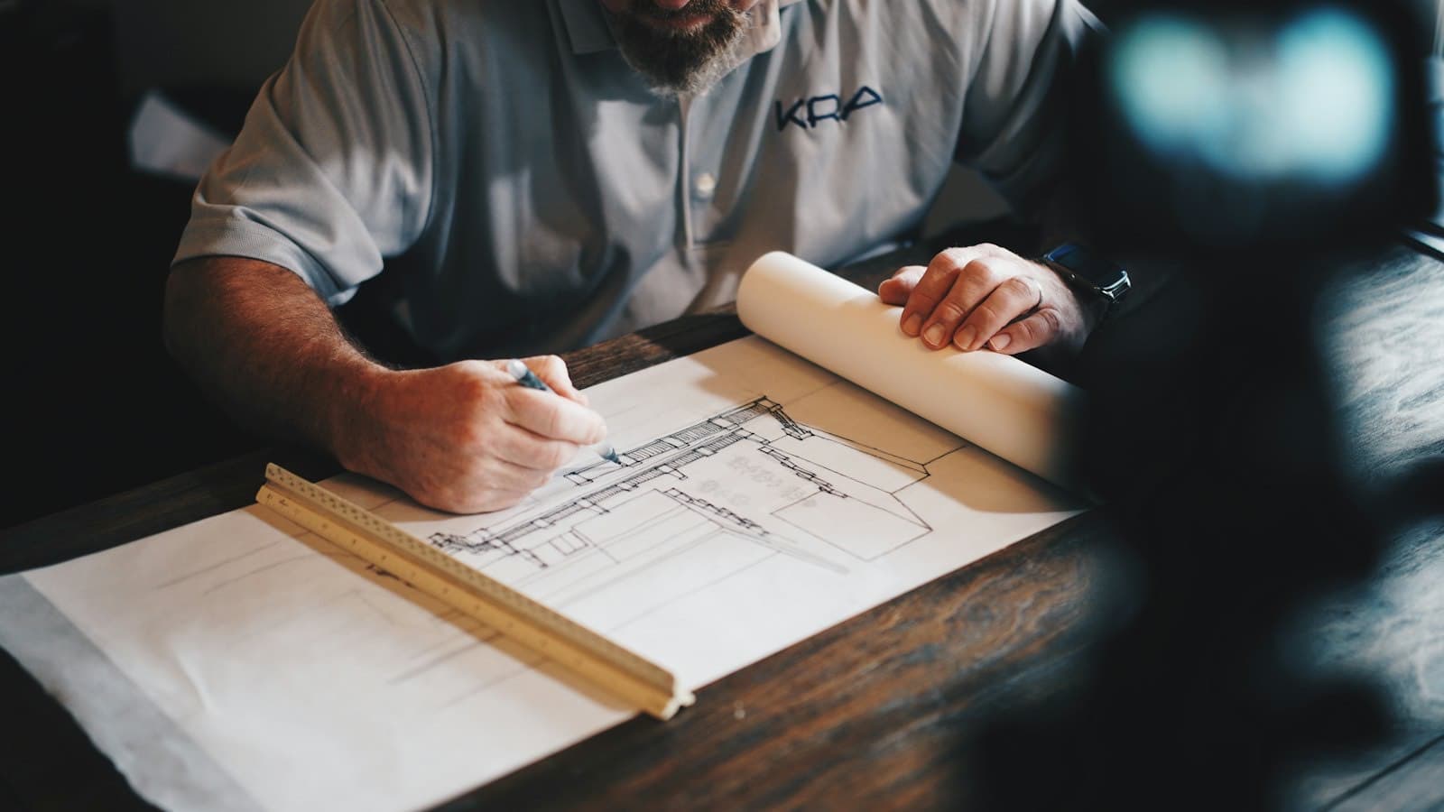 Hands marking up a printed architectural drawing with a pencil and scale ruler